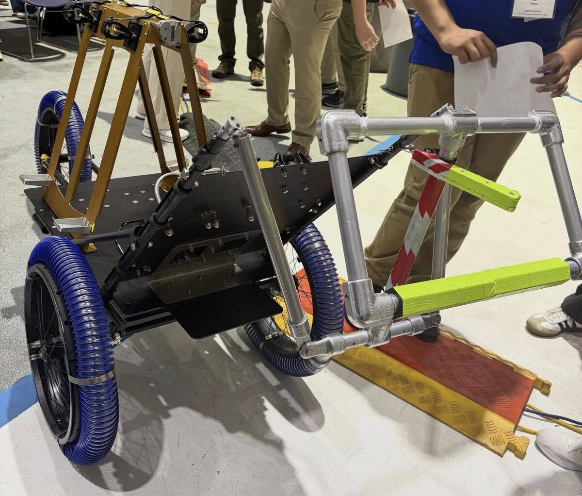 A contraption made out of metal pipes featuring three large blue wheels